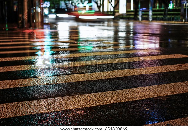 Rainstorm night in the big city, light from the\
shop windows reflected on the road on which cars travel. View from\
the level of asphalt.
