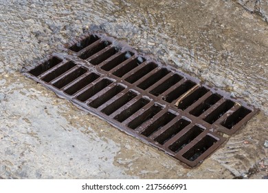 Rainwater Flowing Down The Impervious Concrete Surface To The Storm Drain Equipped With Cast Iron Grid During A Rain
