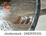 Rainwater flowing over highway storm drain grate. Floodwater and drainage on roads during heavy rain. Flooding on city road with water flowing into storm drains. Sewage management. Selective focus