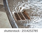 Rainwater flowing over road storm drain grate. Floodwater and drainage on city roads during heavy rain. Flooding on city road with water flowing into storm drains. Sewage management. Selective focus