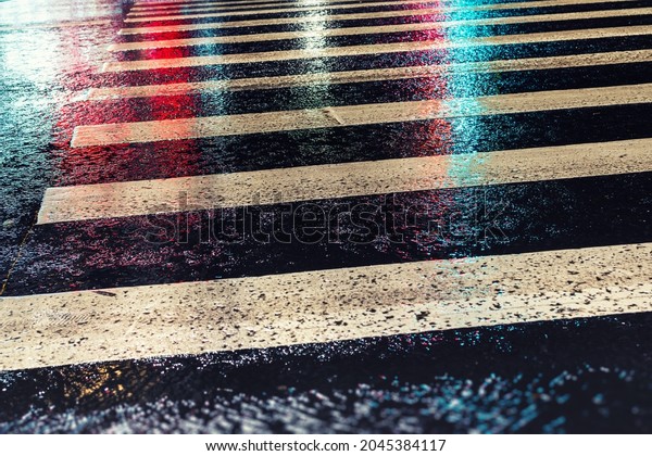 Rainy city street\
reflections on asphalt road crosswalk. City life in night in rainy\
season abstract background. Night asphalt crosswalk as pedesrian\
road safety symbol