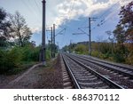 rainy dark clouds above empty railway station with grey broken asphalt and yellow line marking between green trees. Industrial landscape with railroad, colorful cloudy blue sky.
