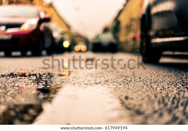 Rainy day in the big city, the cars\
drive along the road. Close up view from the level of the puddle on\
the pavement, image in the orange-blue\
toning