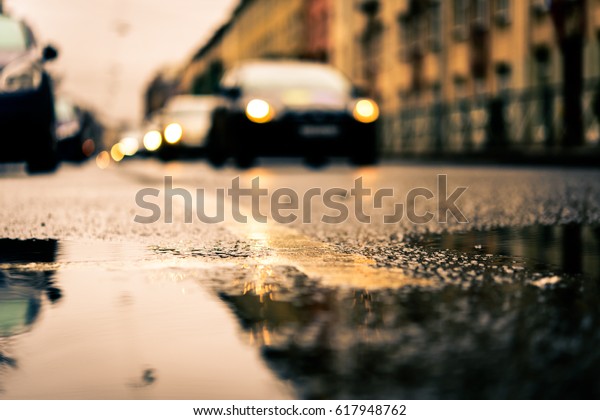 Rainy day in the\
big city, the headlights of the approaching cars. Close up view\
from the puddle level near the dividing line on the asphalt, image\
in the orange-blue toning