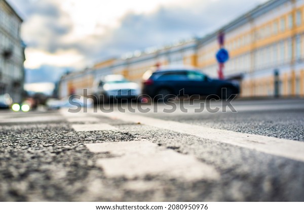 Rainy day in the\
city. Cars drive along the road. Car headlights. Historical center\
of the city. Focus on the asphalt. Close up view from the level of\
the dividing line.