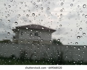 Rainy Day With Clear Droplets On Glass. House, Cement Wall And Green As Background. Selective Focus. Close Up.