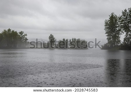 Rainy day: Gray landscape with a pond covered with raindrops and a sky completely obscured by clouds, poor visibility through rain and fog