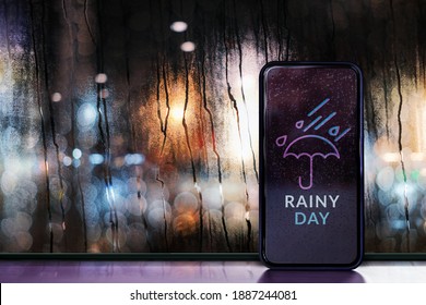 Rainy Day at Night in City Concept. Weather Forecast via Mobile Phone. Raindrops on Glass Window. Blurred Urban Lights as Outside View - Powered by Shutterstock