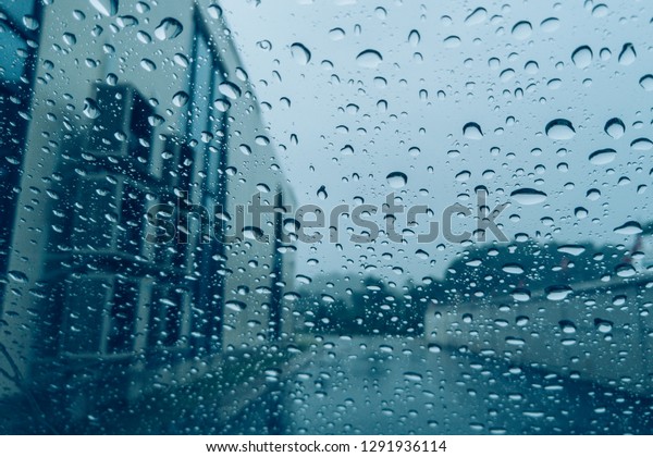 A rainy day view through the car\
windows with rain drops. Blurred background with rain drops on\
glass. Image contains certain grain, noise and soft focus.\
