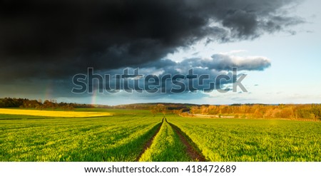Rainy Dramatic Clouds and Rainbow over Fresh Green Spring Field