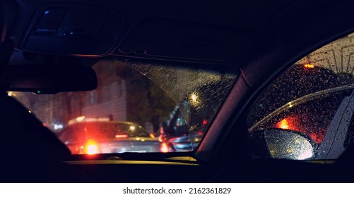 Rainy Glass Dark Blurred Abstract Background Of Auto On Night Road. Water Drops On Car Window With Road Light Bokeh. Car Driving In Night Raining Outside. Car Silhouette Seen Through Wet Windscreen