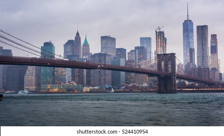  Rainy Manhattan and the Brooklyn Bridge. The tops of the skyscrapers in clouds drown. Night comes to the business district of New York City, the lights. There is rain, heavy fog - Powered by Shutterstock