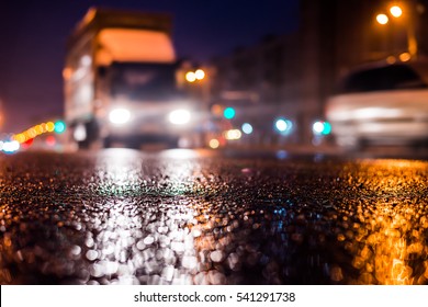 Rainy Night In The Big City, The Approaching Truck Headlights Shine Through The Mist. Close Up View From The Asphalt Level