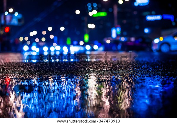 Rainy night in the big city, approaching headlights\
of cars traveling along the avenue.  View from the level of\
asphalt, in blue tones