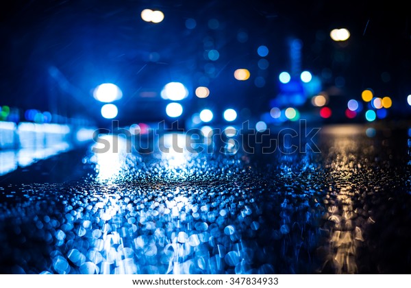Rainy night in the big city, approaching
headlights of car traveling along the avenue. View from the level
of the curb on the road, in blue
tones