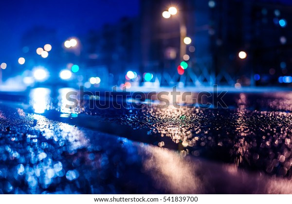 Rainy night in the big city, the\
approaching car headlights shine through the mist. Close up view\
from the level of the dividing line, image in the blue\
tones