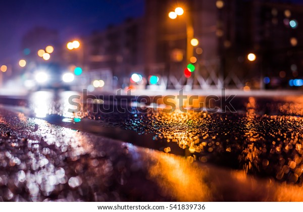 Rainy night in the big city, the approaching car\
headlights shine through the mist. Close up view from the level of\
the dividing line