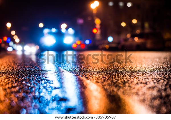 Rainy night in the\
big city, the arriving car on the road. Close up view from the\
level of the dividing\
line