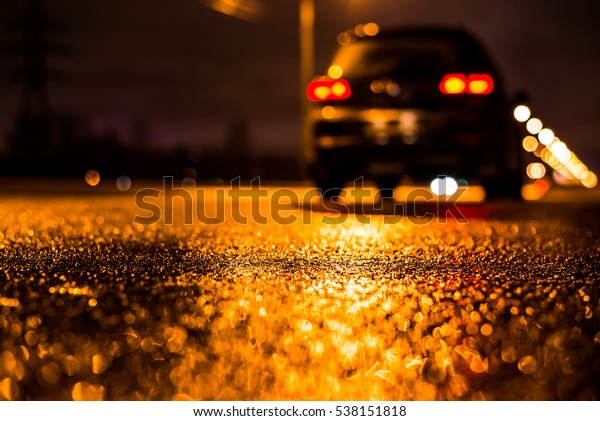 Rainy night in the\
big city, the big black car parked on the roadside. Close up view\
from the asphalt level