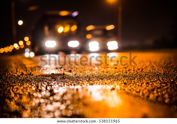 Rainy night in the big city, the blinding headlights\
of the approaching buses. Close up view from the level of the\
dividing line