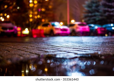 Rainy Night In The Big City, Car Parked Next To The House, Light From The The Windows Of The House. View From The Sidewalk Level Paved With Bricks