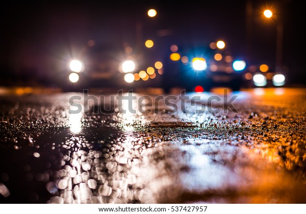 Rainy night in the big city, the car traveling\
towards the headlights illuminate the road. Close up view from the\
level of the dividing\
line