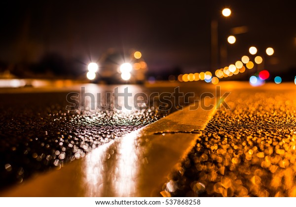 Rainy night in the big city, the car traveling on\
the highway and shines a blinding light. Close up view from the\
level of the dividing\
line