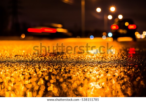 Rainy\
night in the big city, the car parked on the roadside next to pass\
other cars. Close up view from the asphalt\
level