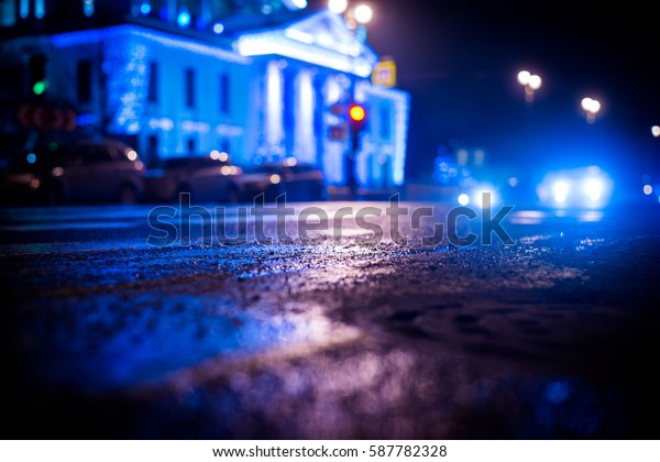 Rainy night in the big city, the\
car rides near the illuminated luxurious mansion. Close up view of\
a hatch at the level of the asphalt, image in the blue\
tones