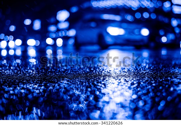 Rainy night in the big city, dense traffic at\
a busy intersection in the light of shop windows. View from the\
level of asphalt, image in the blue\
toning