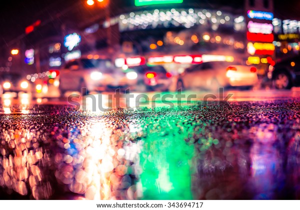Rainy night in the big city,\
dense traffic at a busy intersection in the light of shop windows.\
View from the level of asphalt, image in the soft orange-purple\
toning