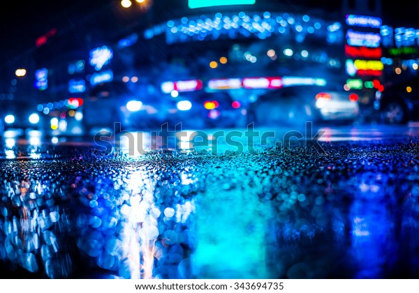 Rainy night in the big city, dense traffic at a\
busy intersection in the light of shop windows. View from the level\
of asphalt, in blue tones