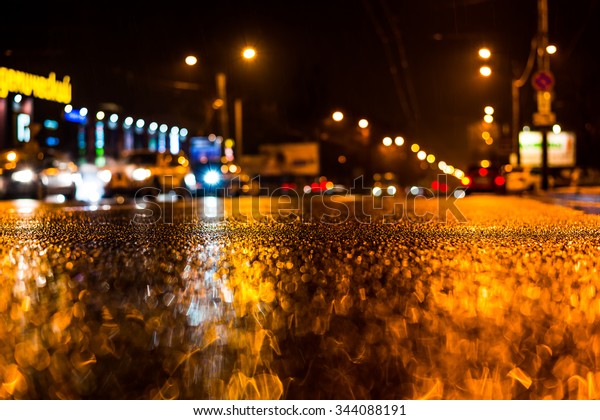 Rainy\
night in the big city, dense traffic at a busy avenue in the light\
of shop windows. View from the level of\
asphalt