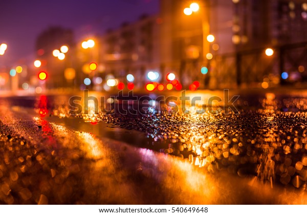 Rainy night in the\
big city, the empty road with puddles. Close up view from the level\
of the dividing line