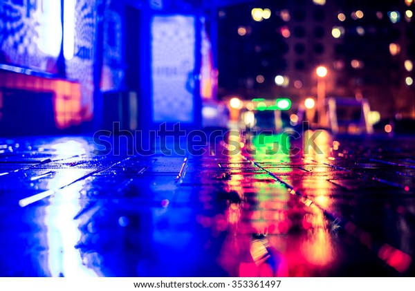 Rainy\
night in the big city, light from the night club and the windows of\
the house is reflected in the asphalt. View from the sidewalk level\
paved with bricks, image in the yellow-blue\
toning