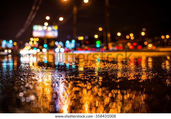 Rainy\
night in the big city, the light from the headlamps of approaching\
car on the highway. View from the level of\
asphalt