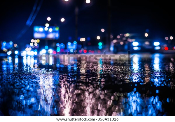 Rainy night in the big city, the light from the\
headlamps of approaching car on the highway. View from the level of\
asphalt, in blue tones
