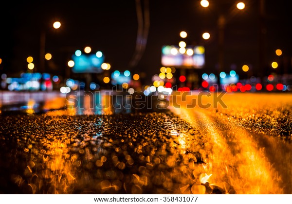 Rainy night in the big city, the light from the\
headlamps of vehicles approaching on the highway. View from the\
level of the dividing\
line