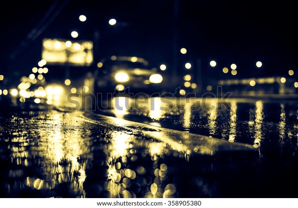 Rainy night in the big city,\
the light from the headlamps of approaching car on the highway.\
View from the level of the dividing line, image in the yellow-blue\
toning