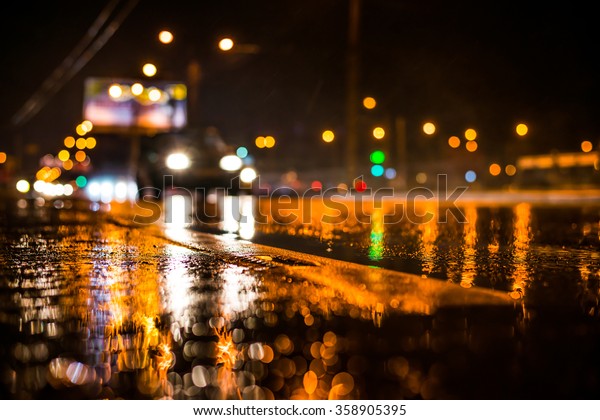 Rainy night in the big city, the light from the\
headlamps of approaching car on the highway. View from the level of\
the dividing line