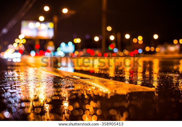 Rainy night in the big city, the light from the\
headlamps of vehicles approaching on the highway. View from the\
level of the dividing\
line
