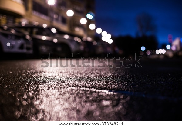 Rainy night in the big city, the\
light from the lanterns in the courtyard of the house in which the\
parked cars. View from the level of asphalt, in blue\
tones