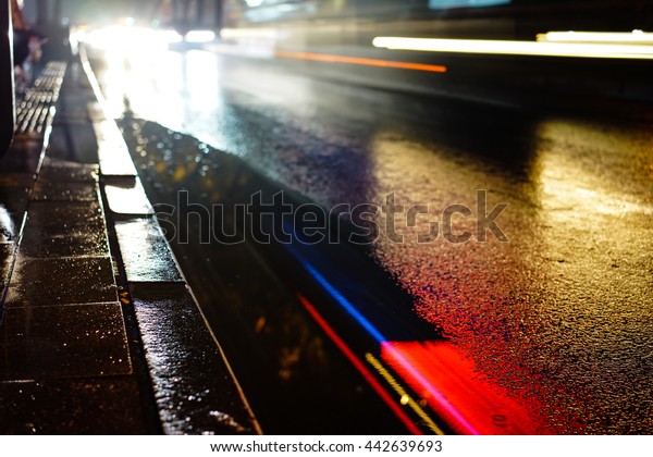 Rainy night in the big city, the\
light from the headlamps of vehicles approaching on the road. Close\
up view from the level of asphalt,  focus on the\
asphalt