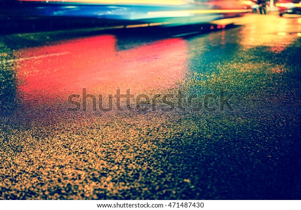 Rainy night in the big city, the\
light from the headlamps of vehicles approaching on the road. Close\
up view from the level of asphalt, focus on the\
asphalt