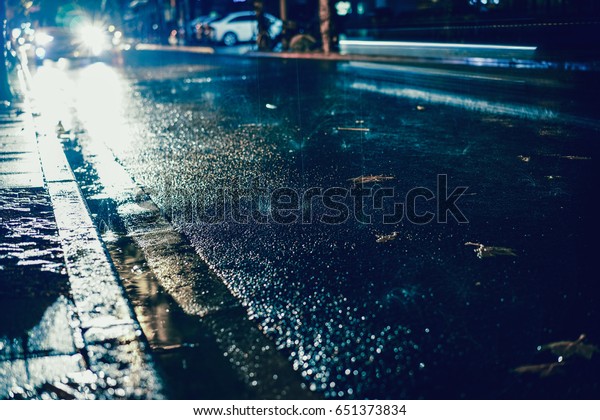 Rainy night in the big city, light from the shop\
windows reflected on the road on which cars travel. View from the\
level of asphalt