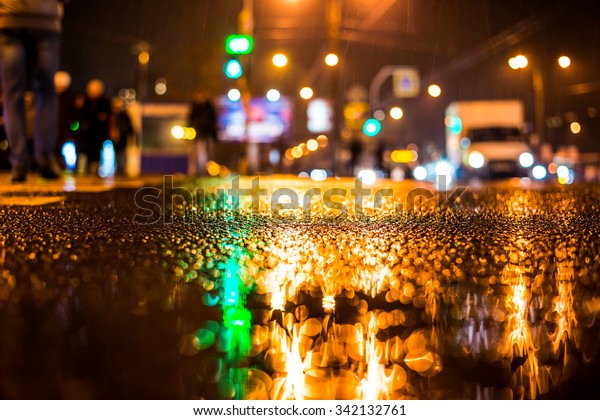 Rainy night in the big\
city, pedestrians cross the busy intersection. View from the level\
of asphalt