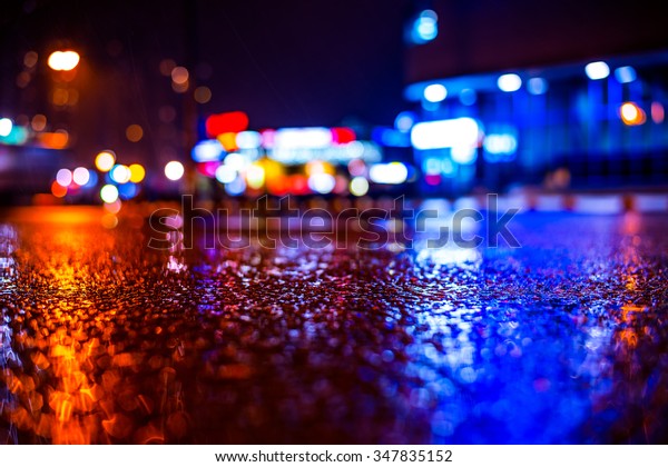 Rainy night in the\
big city, road in the light of shop windows. View from the level of\
asphalt, in blue tones