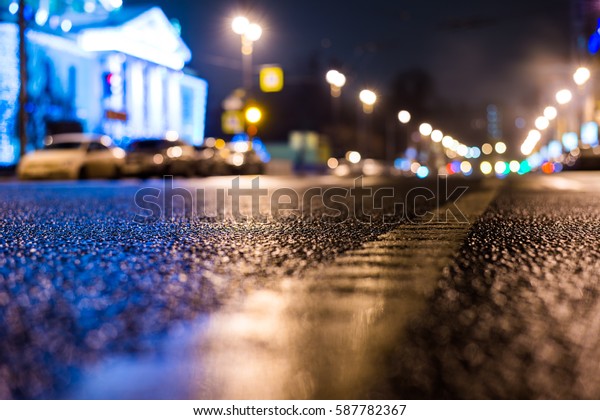 Rainy night in the big\
city, the road passes next to the illuminated luxurious mansion.\
Close up view from the level of the dividing line, image in the\
blue tones