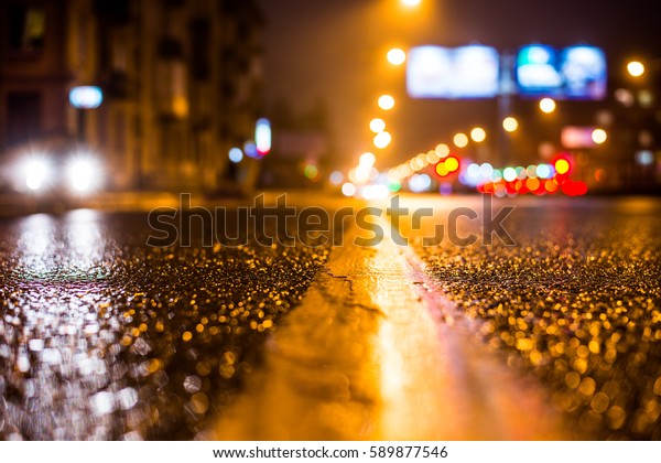 Rainy night in the big city, the road lighting\
lanterns and headlights of the approaching cars. Close up view from\
the level of the dividing\
line
