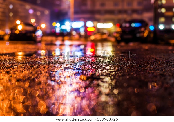 Rainy night in\
the big city, the street with bright shop windows. Close up view of\
a puddle on the asphalt\
level